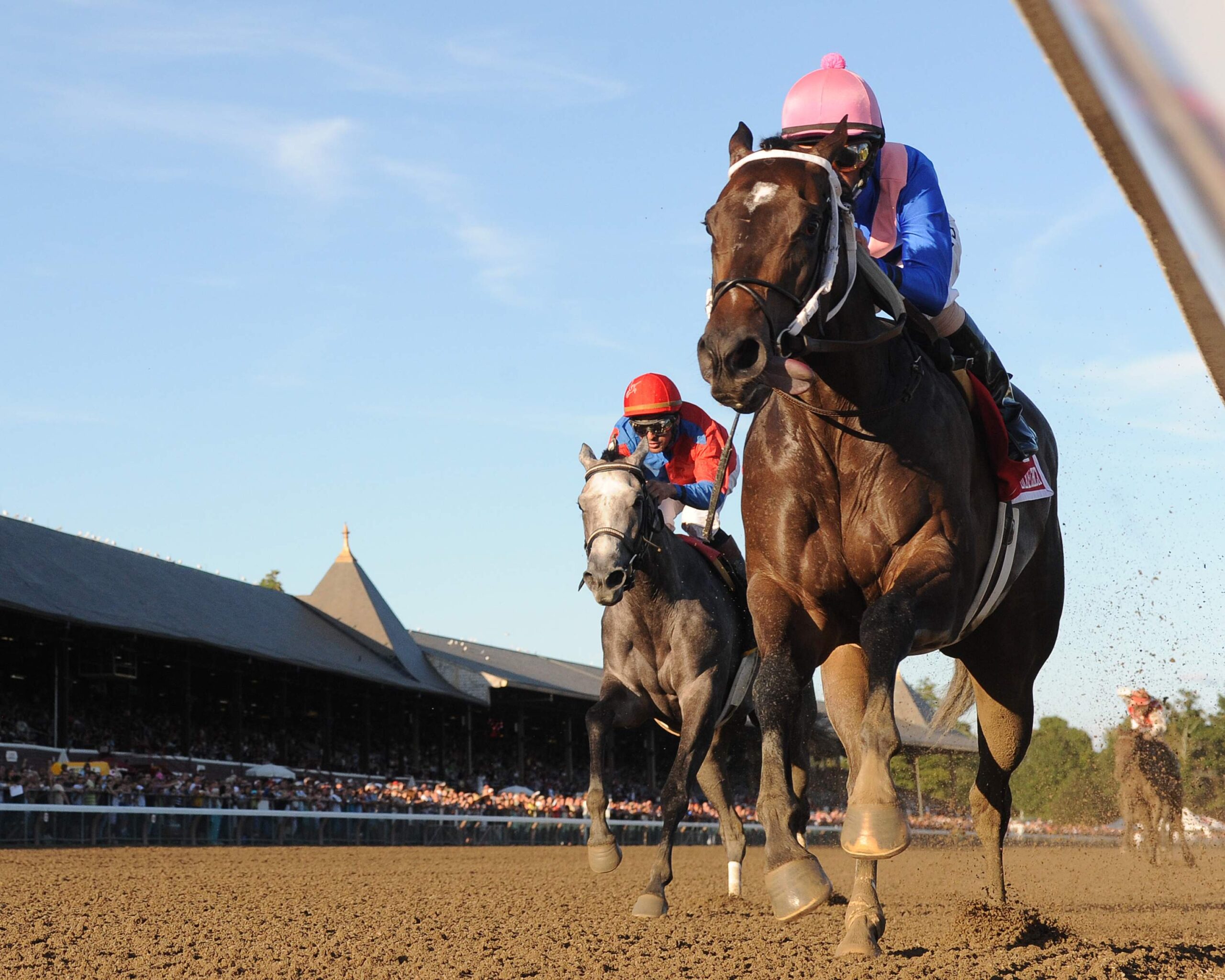 Horses racing on dirt track at sunset.